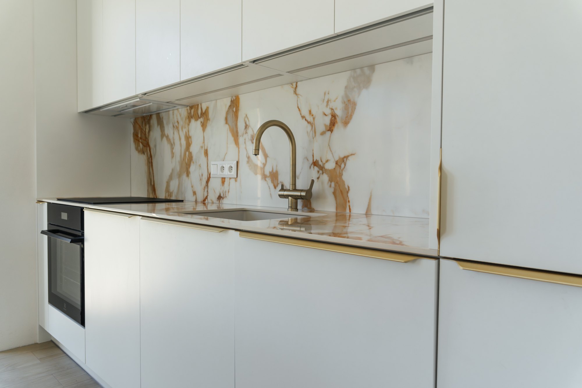 White kitchen made of laminated chipboard with gold handles, ceramic worktop with marble decor and a built-in oven, Čunovo.