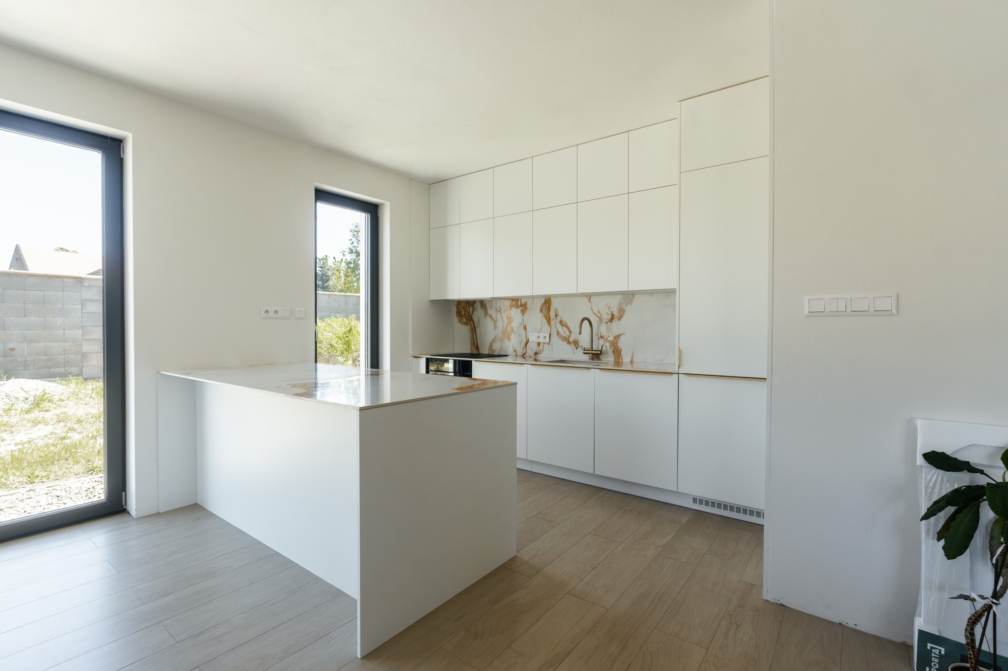 White kitchen with an island, tall floor-to-ceiling units and a ceramic worktop in marble decor, Čunovo.