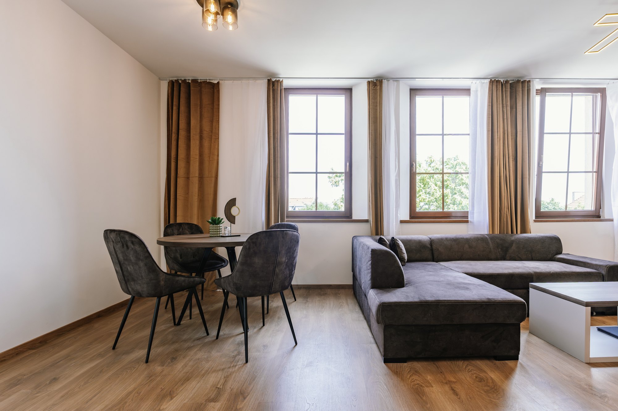 A living room with a U-shaped Cashmere Grey sofa and a round dining table with chairs in Cashmere Grey, flooring in Brown Warmia Walnut, Bratislava.
