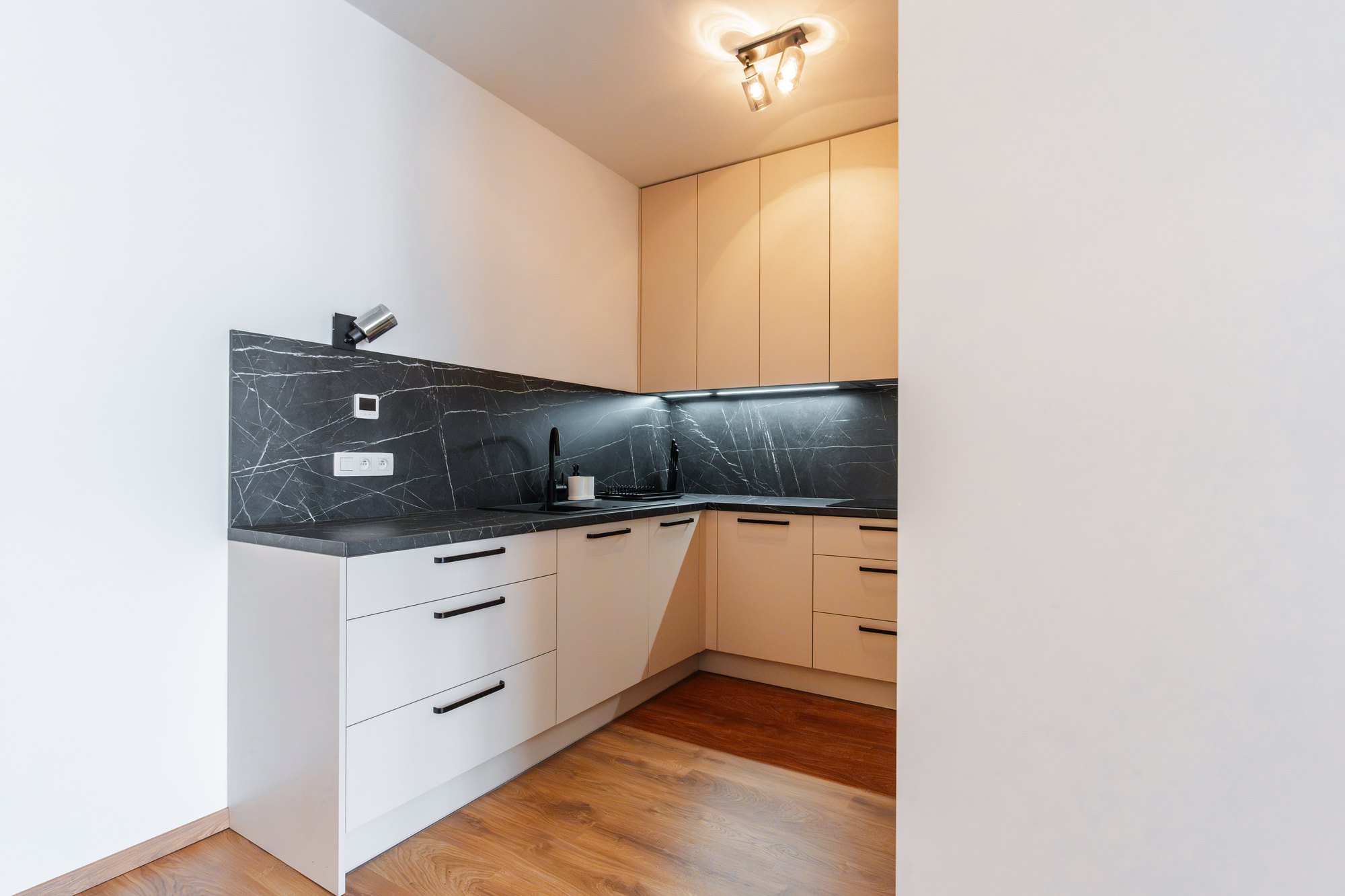 Kuchynská linka v tvare L s bielo-béžovými skrinkami, pracovnou doskou a zadnou stenou v dekore čierneho mramoru Pietra Grigia, Bratislava.