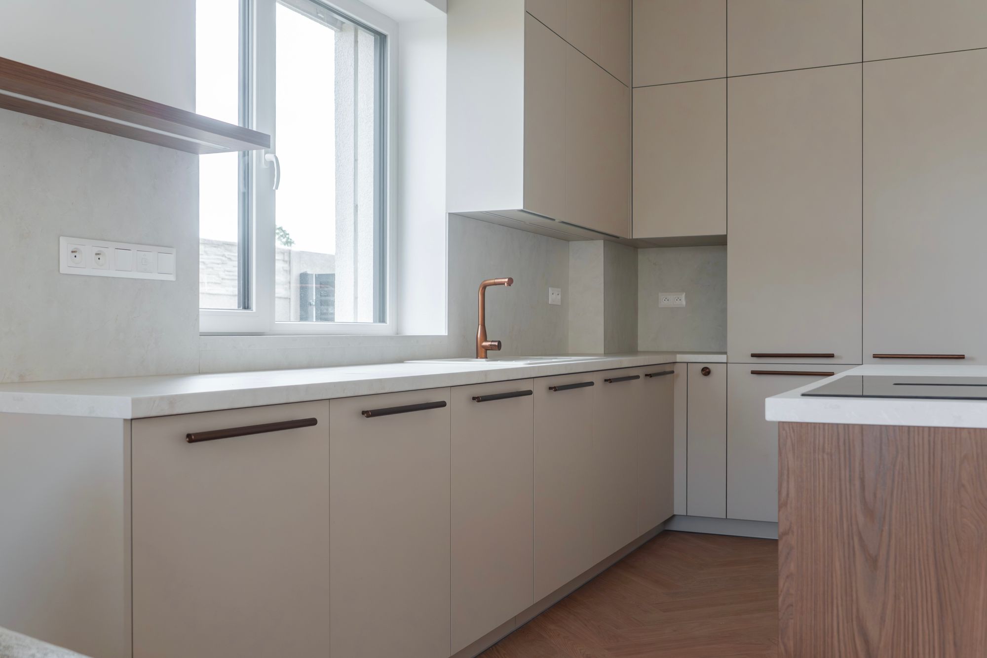 Kitchen unit in cashmere with tall floor-to-ceiling cabinets and an island in Brown Casella Oak, copper tap and white worktop, Rovinka.