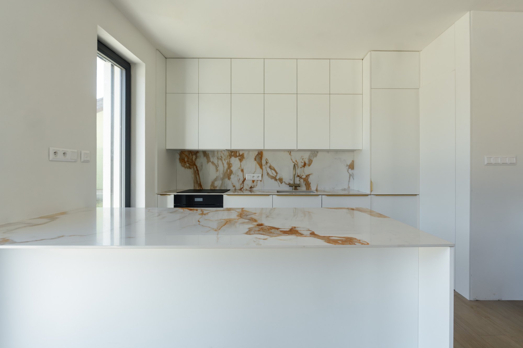 Bespoke white kitchen with an island and tall floor-to-ceiling units, ceramic worktop with marble decor, Čunovo.
