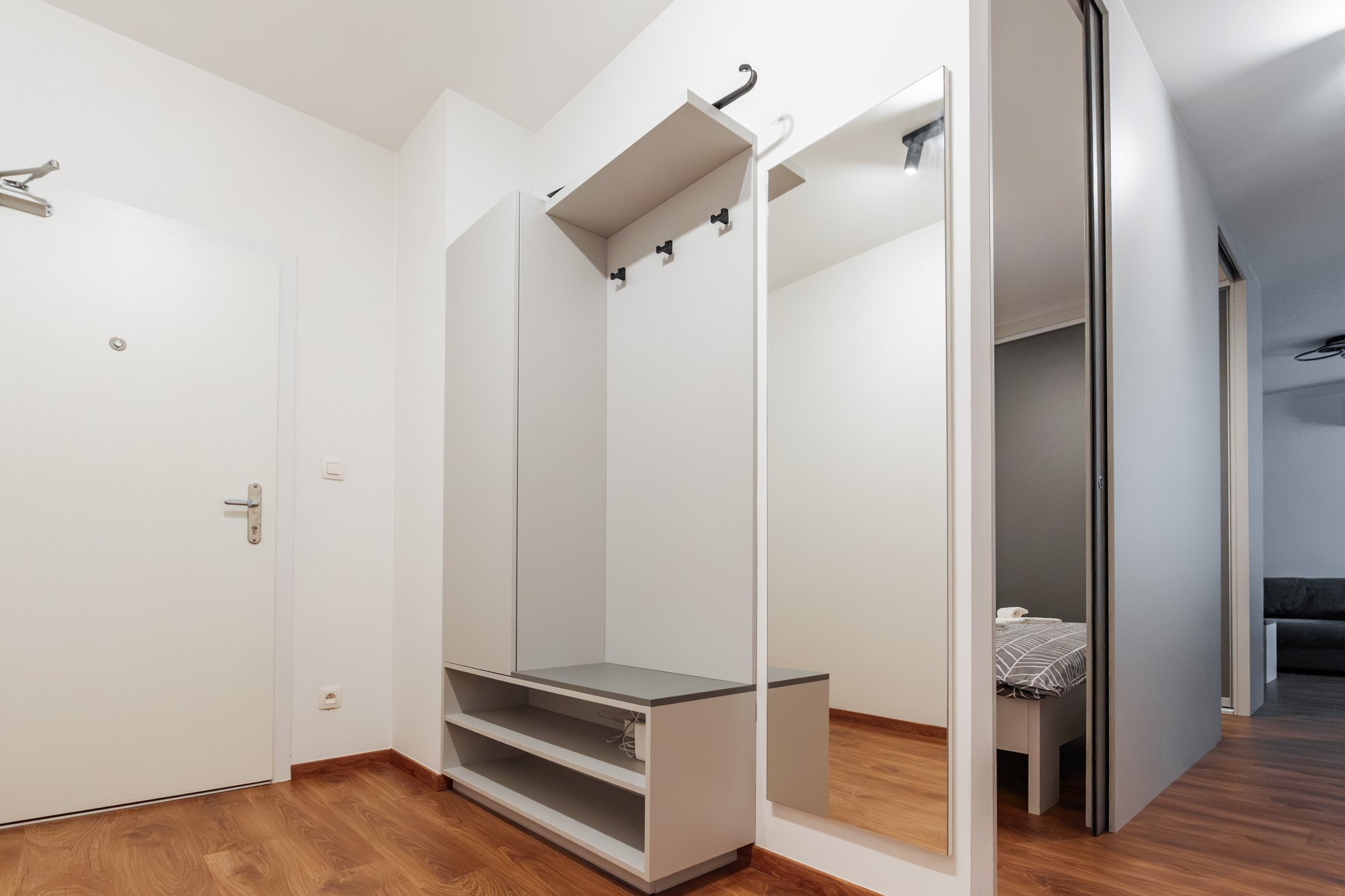 Built-in wardrobe unit in dusty grey laminate with a shoe bench, hooks and a large mirror in the hallway, Bratislava.