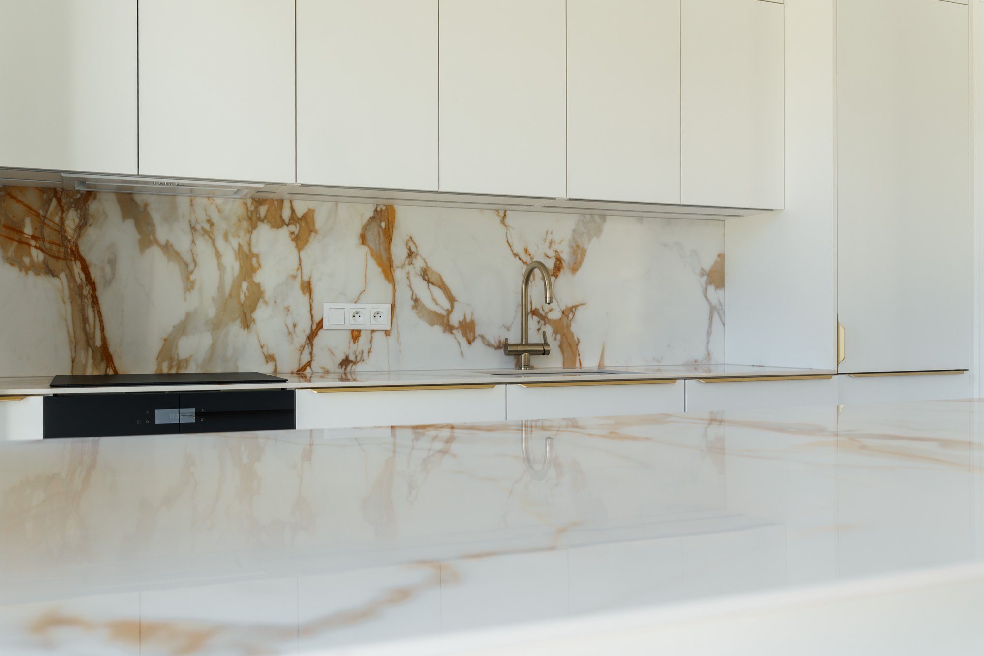 White kitchen with a marbled ceramic worktop and upstand, gold details and a built-in sink, Čunovo.