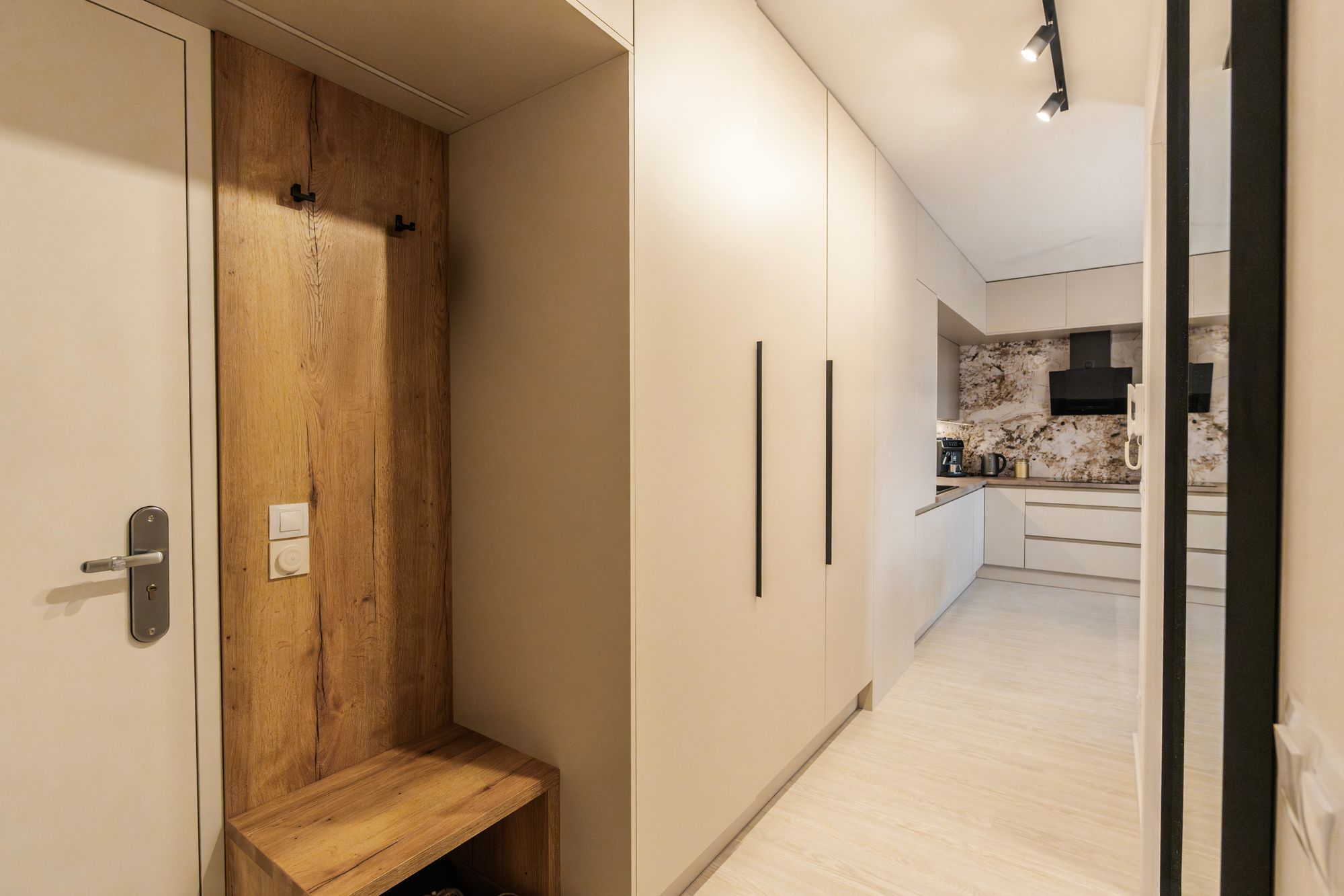 A built-in hallway cupboard with wood veneer and a bench leads into the kitchen in Cashmere Grey with a Titanit worktop, Bratislava.
