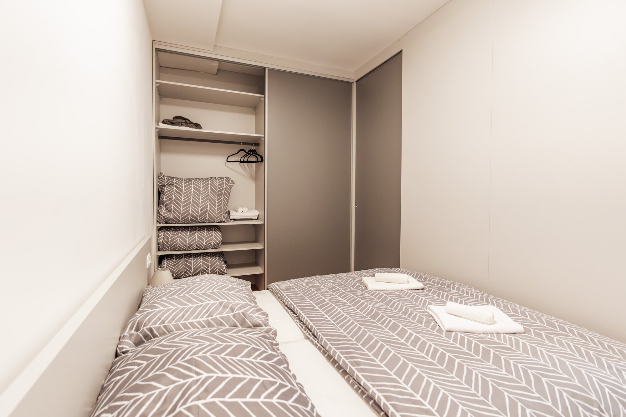 Built-in wardrobe with grey sliding doors and open shelves in the bedroom, laminated chipboard in dusty grey, Bratislava.